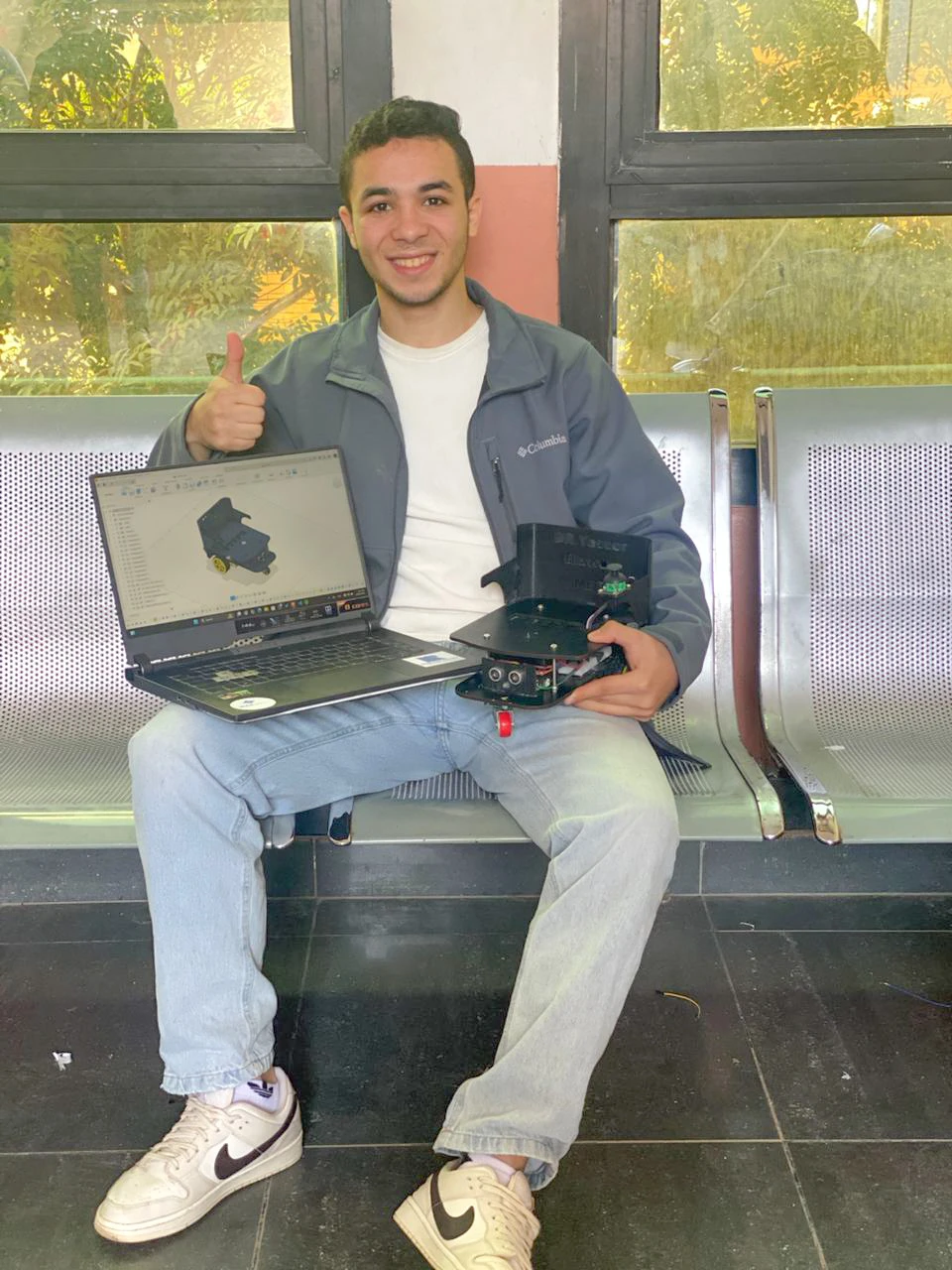 Mohamed Sakr holding laptop with Fusion 360 robot design and physical prototype — Sakr Makes engineering and maker project